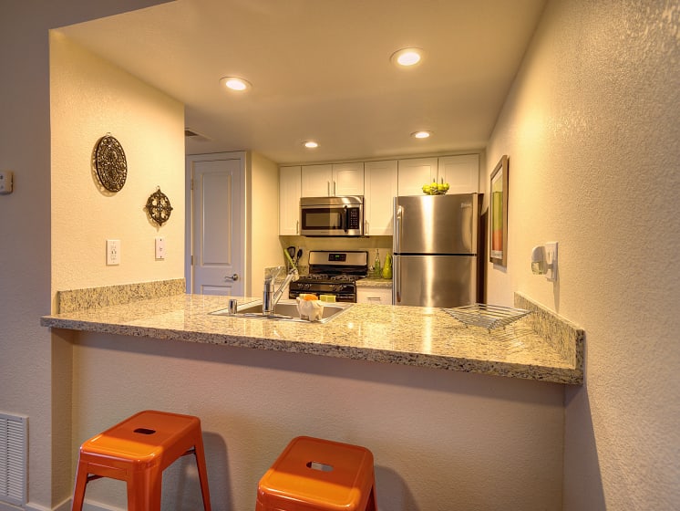 Kitchen Bar Seating with Orange Stools, Granite Countertop, Sink, Refrigerator and Microwave